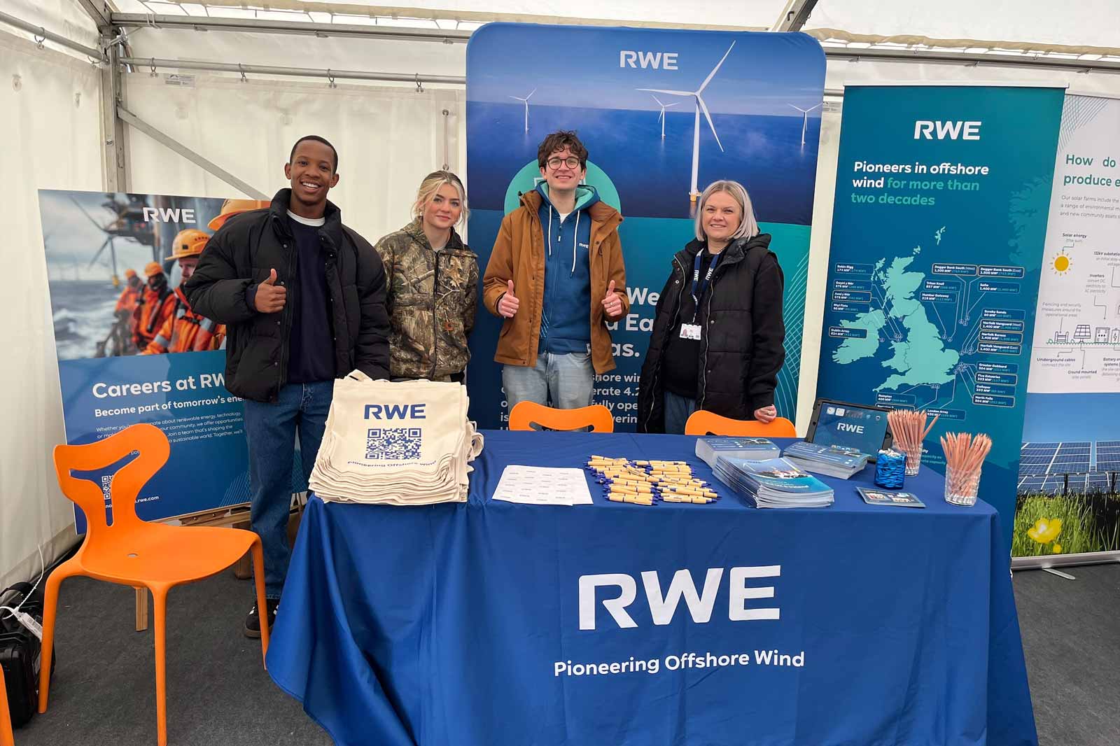 Four people stand at an RWE booth showcasing offshore wind power, with promotional materials on a blue table.